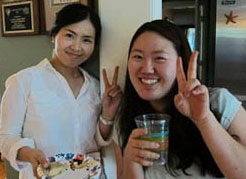 Two international women at party in a private home. Both are making the peace sign with two fingers.