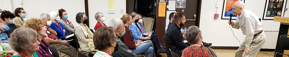 Audience of masked CCIS members listening to a bend forward lively male speaker.