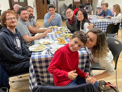 Group of happy male and female diners around a table eating. A mother and son in the foregound.