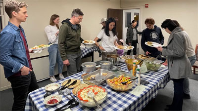 Group of seven diners serving themselves dinner from a table full of food.